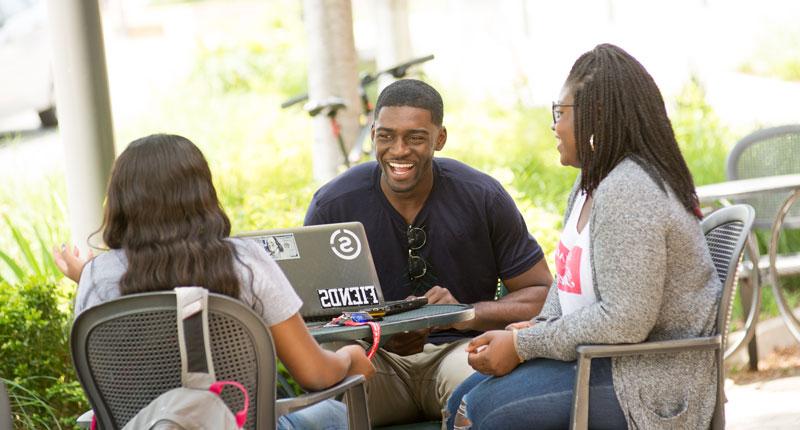 Three students chat at a table outside the Coffee Hound.